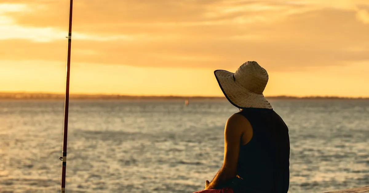 10月の朝マズメ - 釣り竿を持ち夕焼けの海を眺めるアングラー